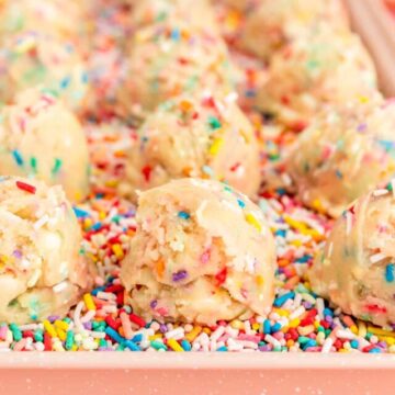 Close up of cookie dough scoops and pink tray filled with sprinkles.