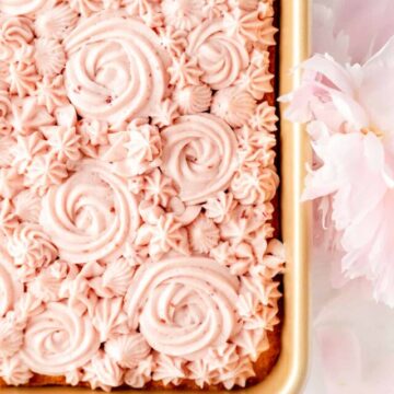 Overhead of raspberry cream cheese frosting swirled on vanilla sheet cake surrounded by flowers.