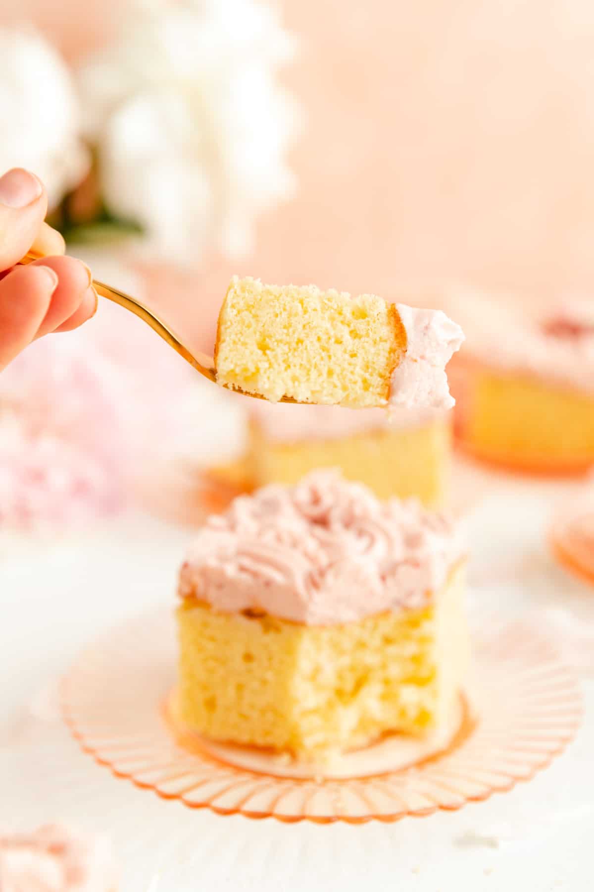 Hand with Gold Fork holding a bite of vanilla sheet cake with raspberry frosting..