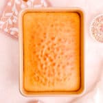 Overhead of golden vanilla sheet cake in gold pan on pink background.