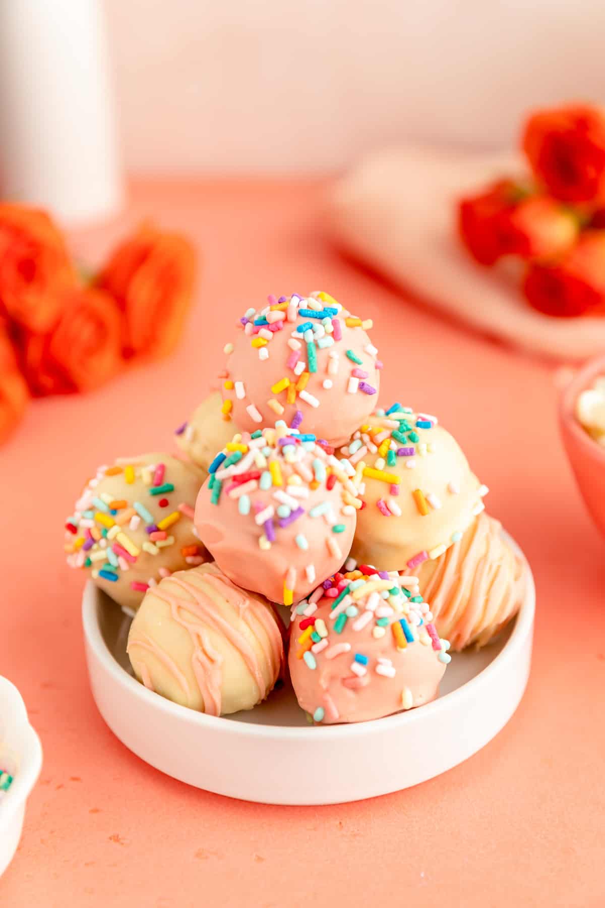 A white dish filled with pink white and sprinkle covered cookie dough truffles.