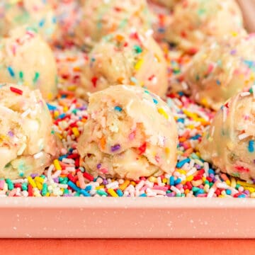 Close up of cookie dough scoops and pink tray filled with sprinkles.