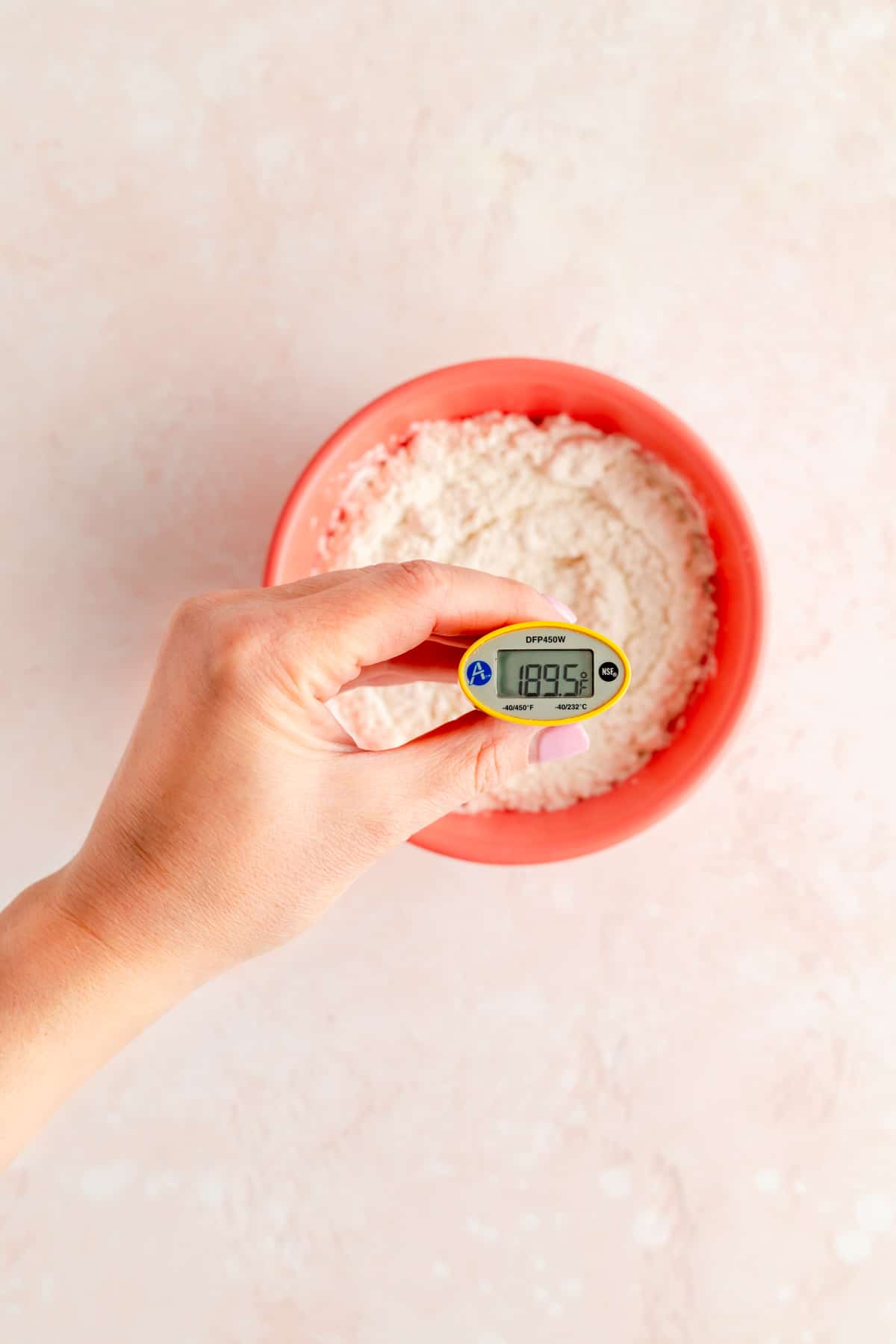 Hand holding thermometer reading 189.5 in pink bowl filled with flour.