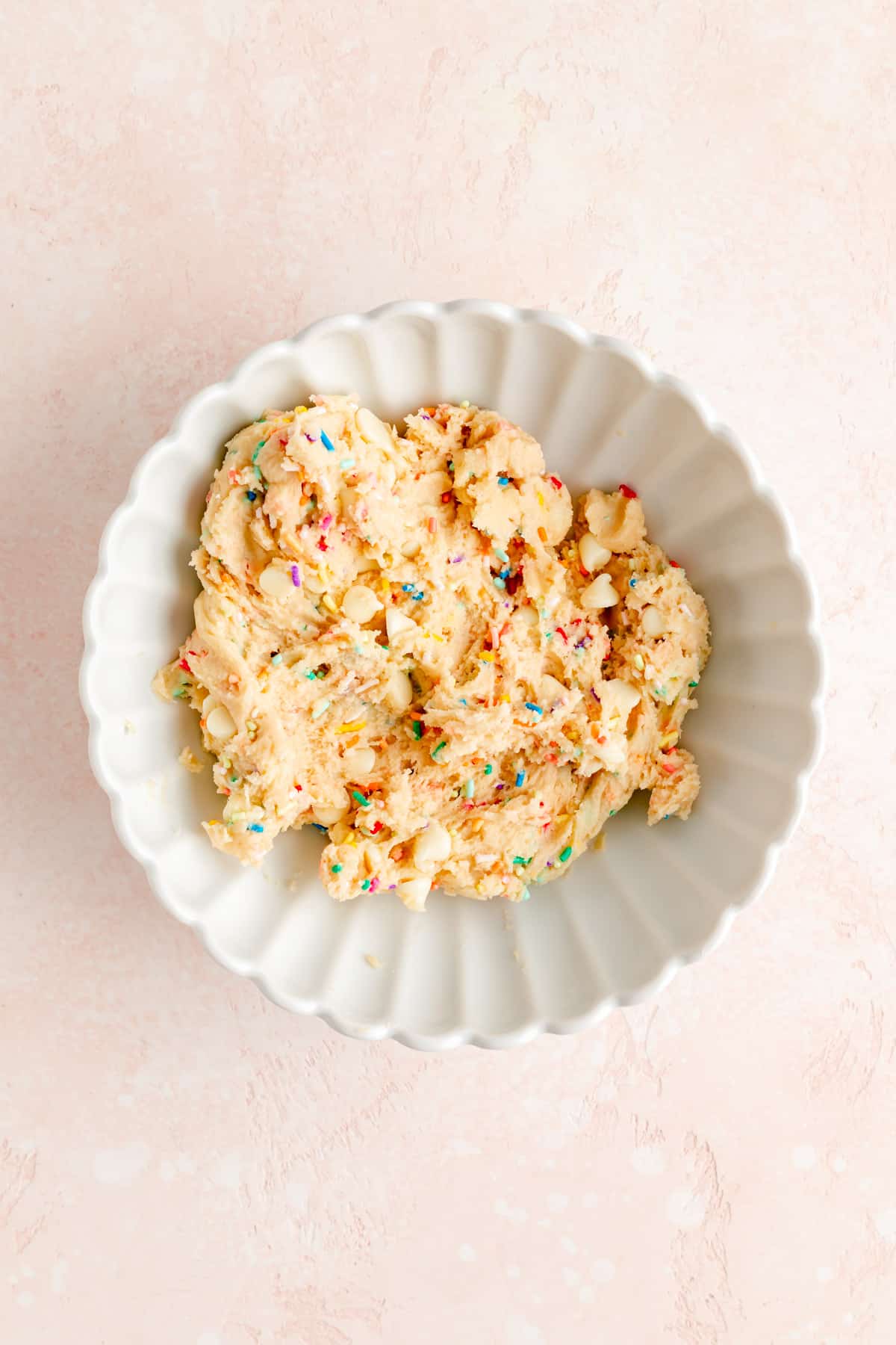 White scalloped mixing bowl filled with finished edible funfetti sugar cookie dough.