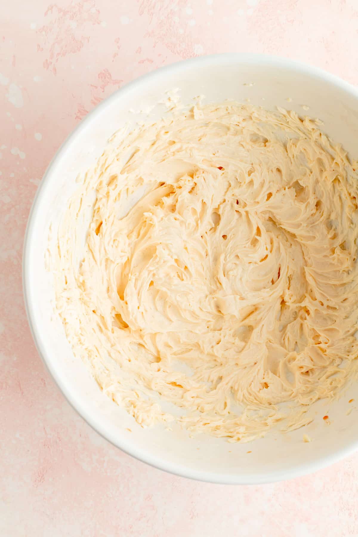 Overhead of whipped cream cheese butter and vanilla in white bowl on pink background.
