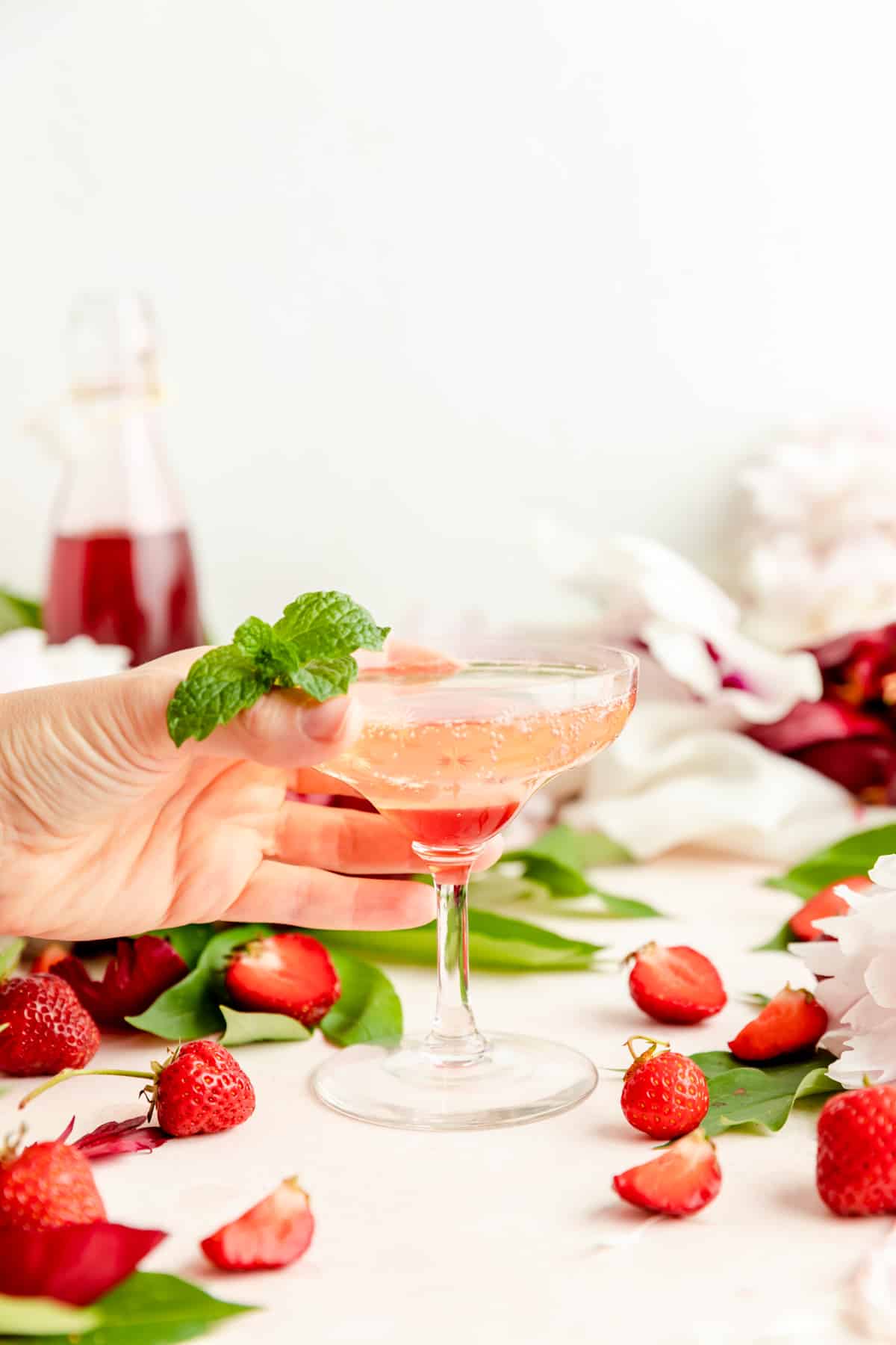 And grabbing pink and red cocktail glass with mint sprig on table with berries.