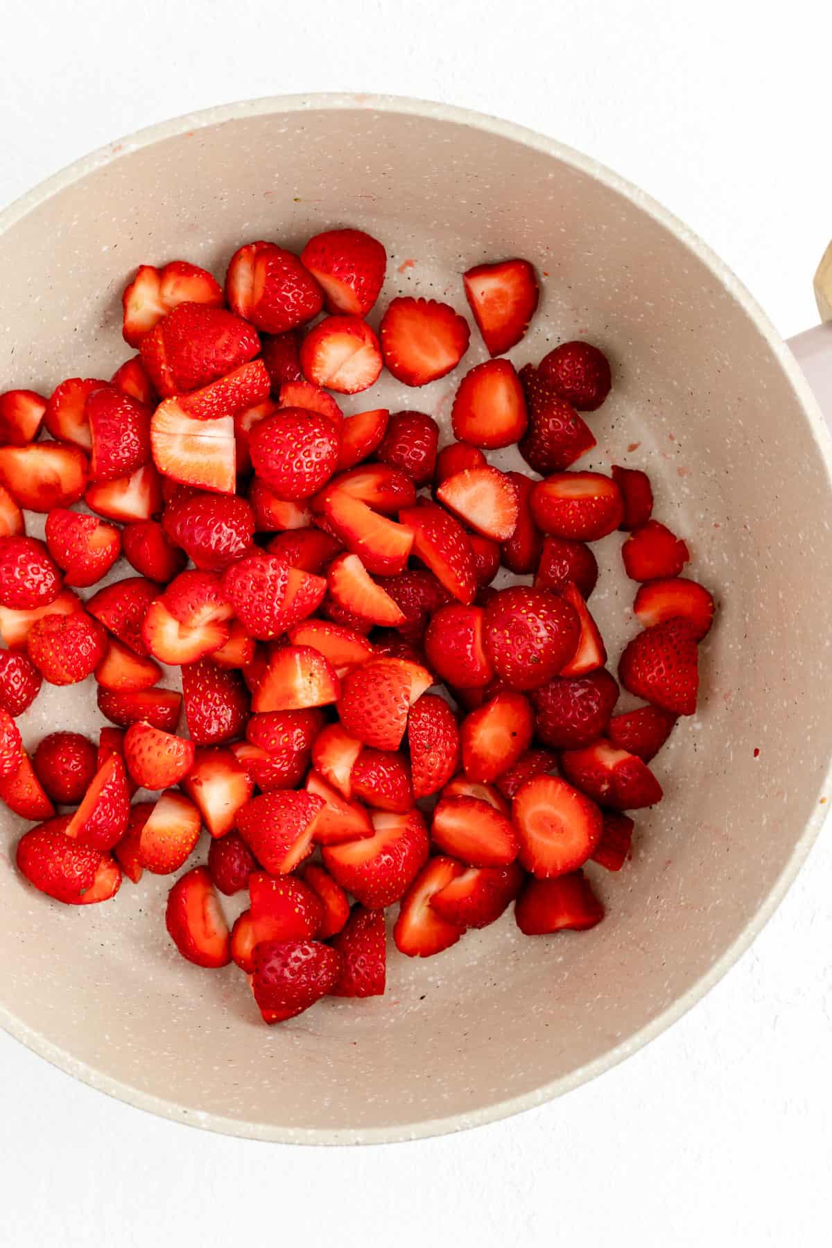 Quartered and de-topped strawberries in tan pot from above.