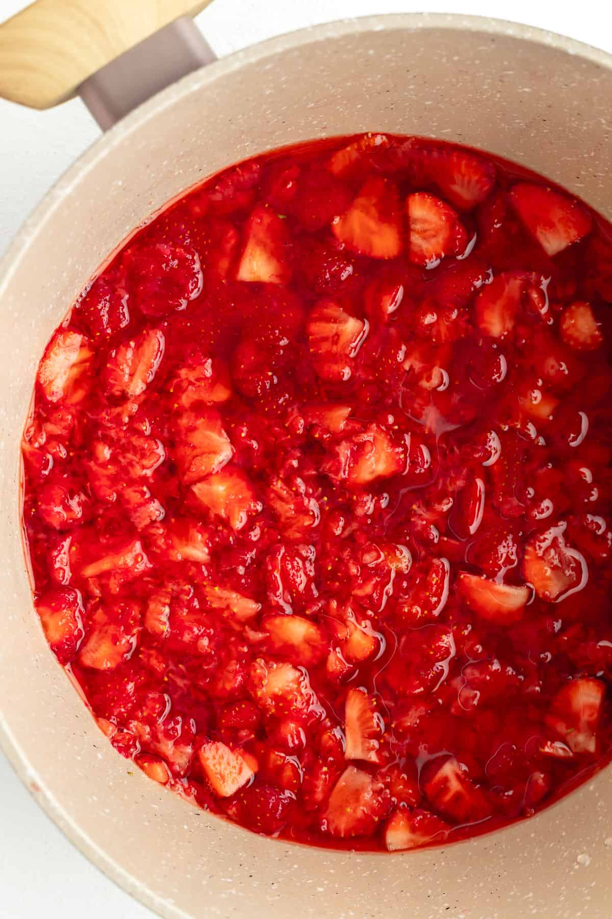 Overhead of strawberries mashed in water in tan pot.
