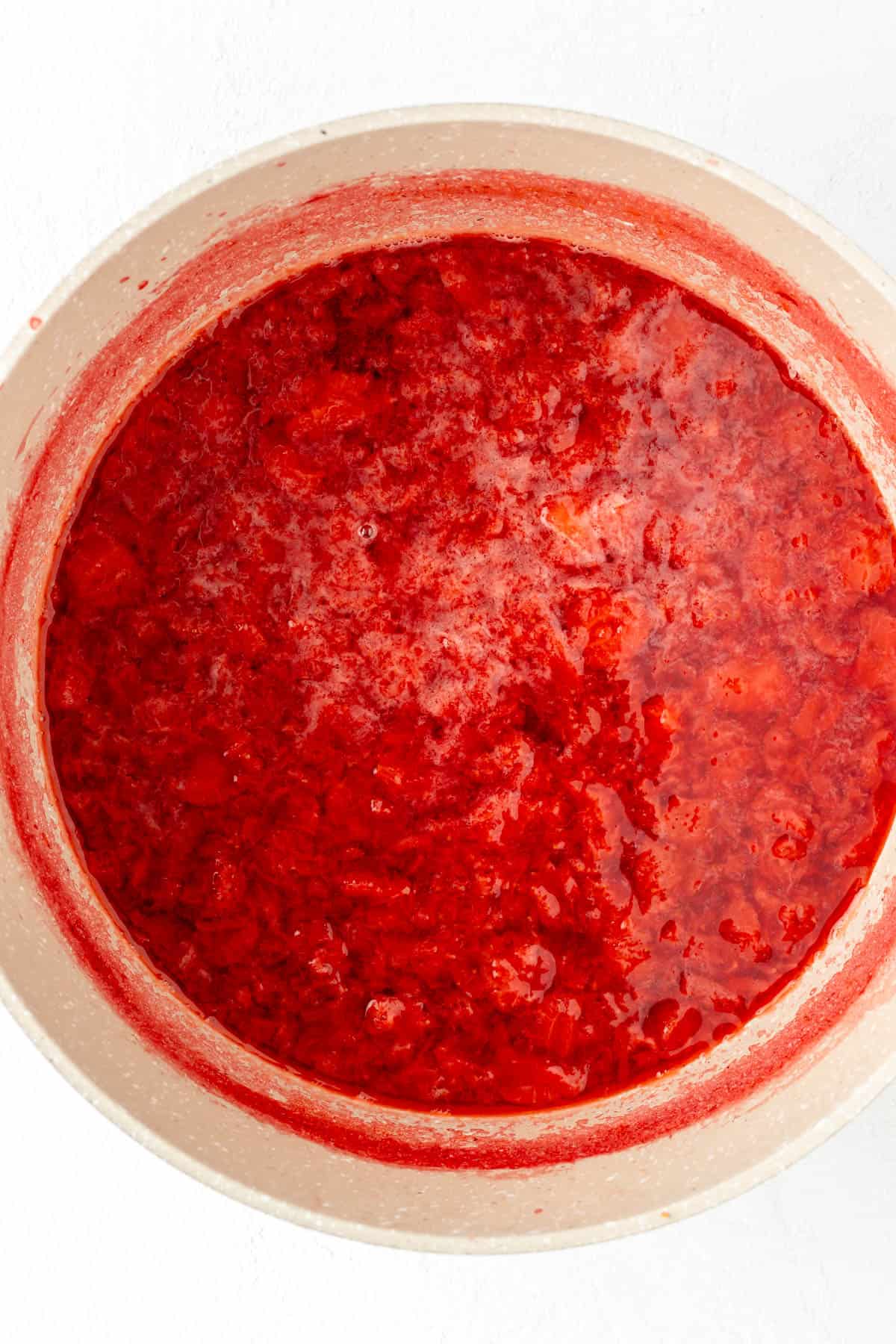 Overhead shot of boiled strawberries in water in tan pot.