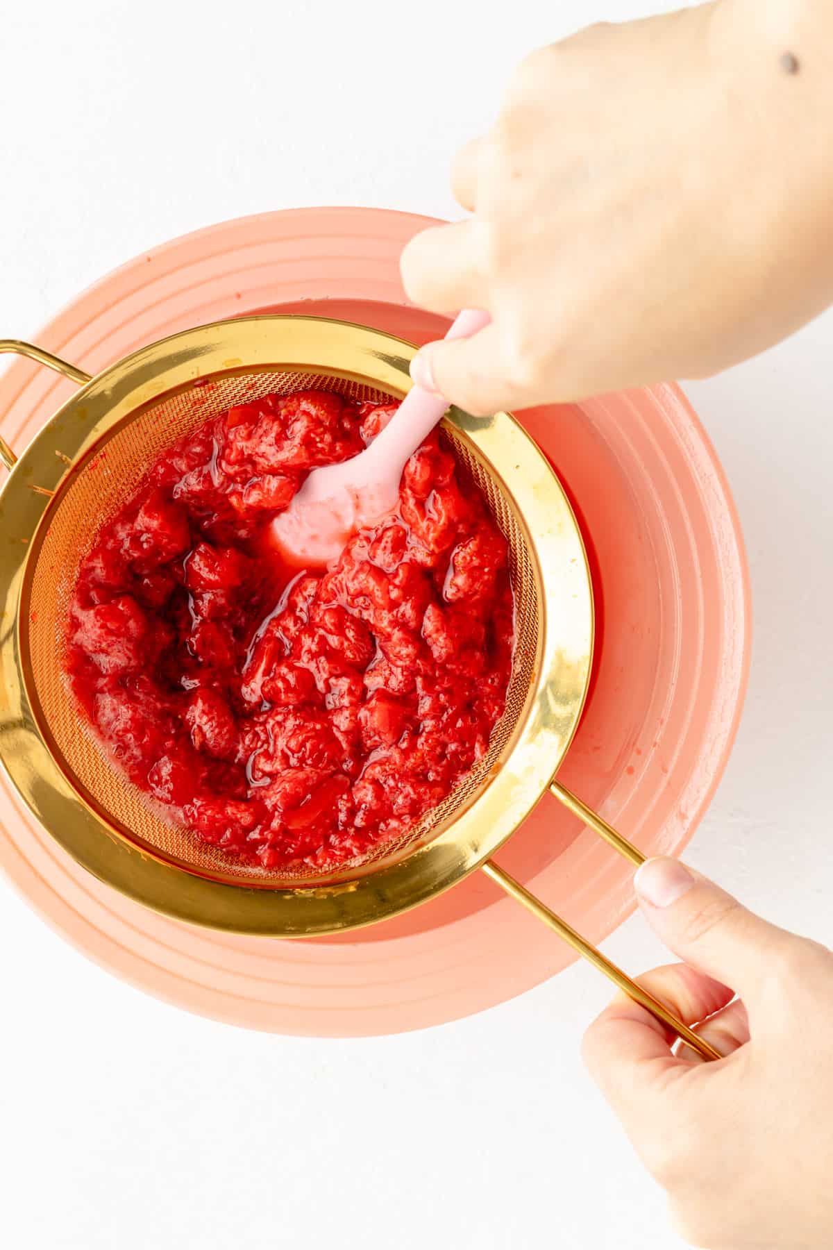 Overhead view of oiled strawberries and water being streamed through gold sieve.