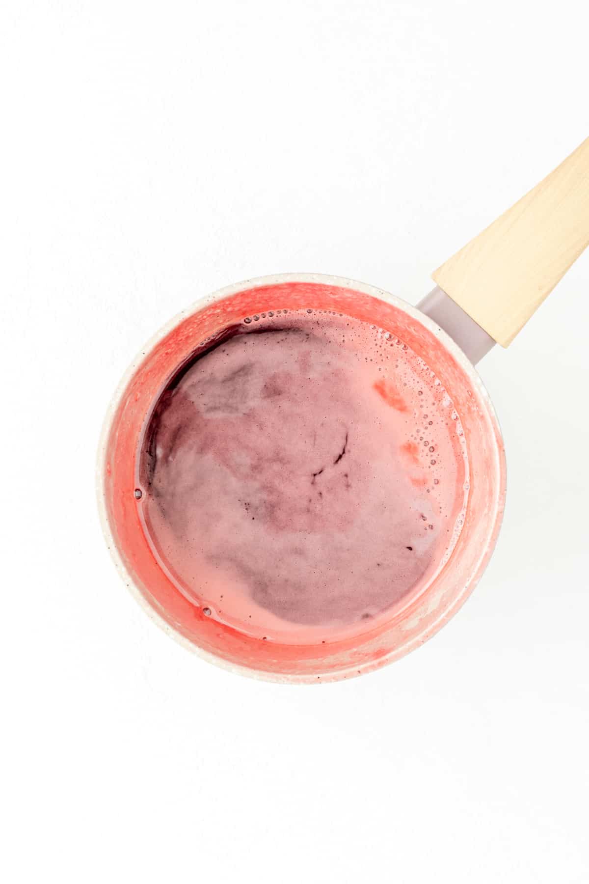 Overhead shot of pot filled with strawberry simple syrup covered in foam.