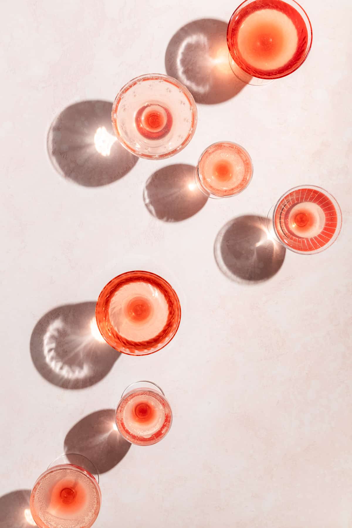 Six Crystal cocktail glasses with pink liquid and dark angled shadows.