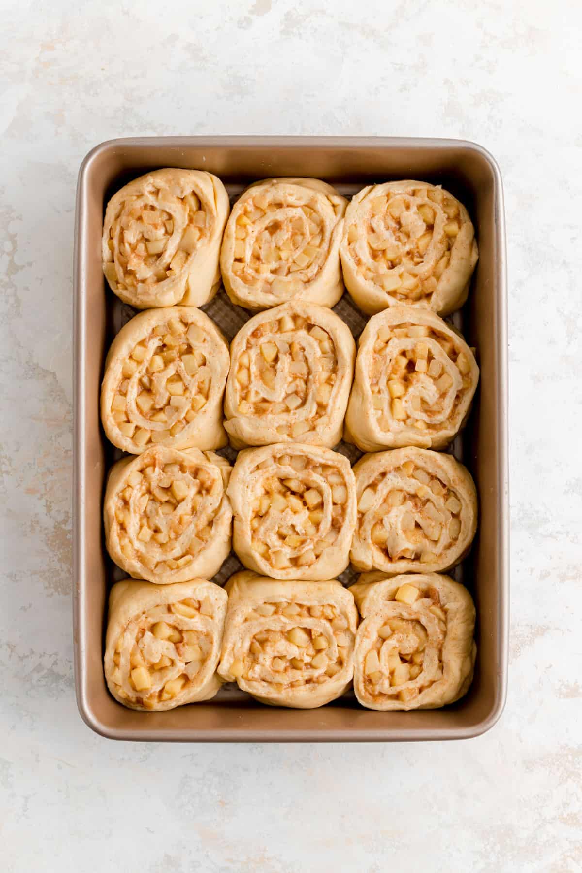 sliced cinnamon rolls with apple pie filling arranged in a 9 by 13 inch pan.