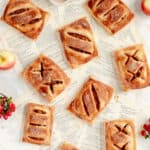 a bunch of apple hand pies on torn out recipe pages with red berries and apples.