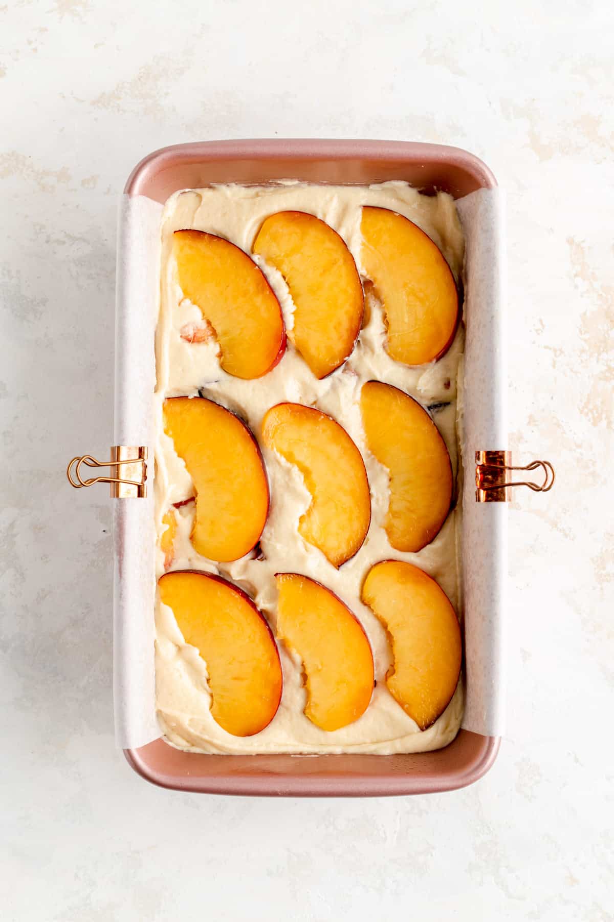 Nine peach slices on top of raw peach pound cake batter in pink loaf pan.