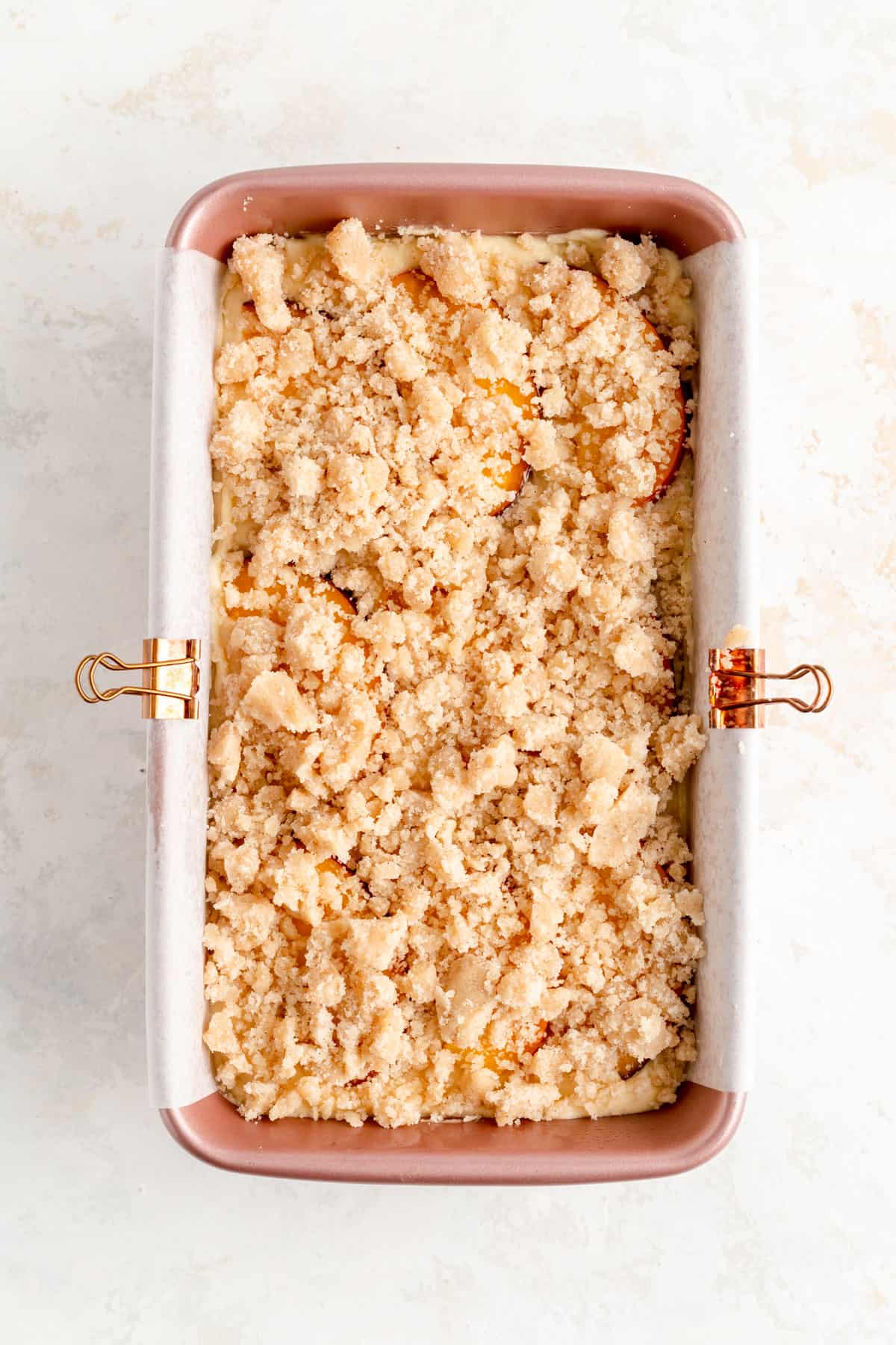 Streusel covered raw peach cobbler pound cake batter in pink loaf pan.