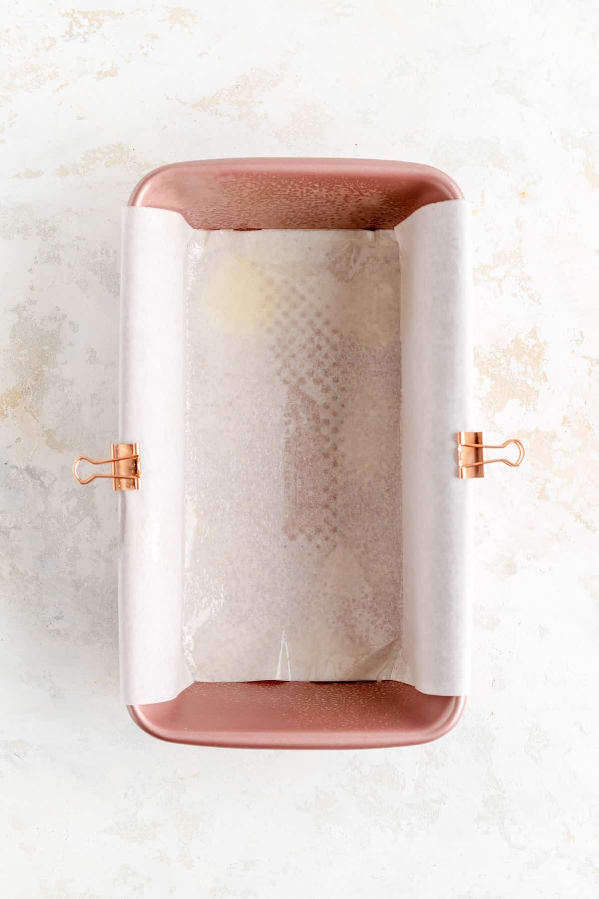 pink loaf pan lined with parchment paper secured with copper alligator clips.