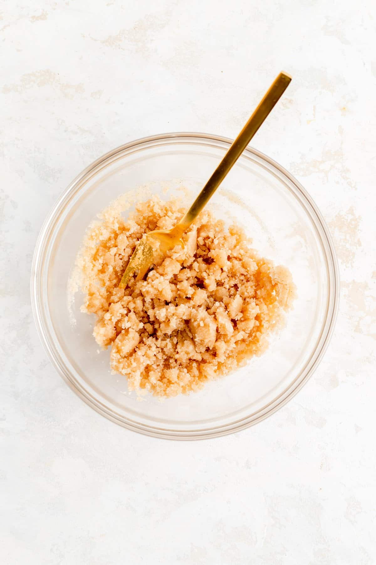 a bowl of cinnamon streusel topping with gold fork in it on white background.