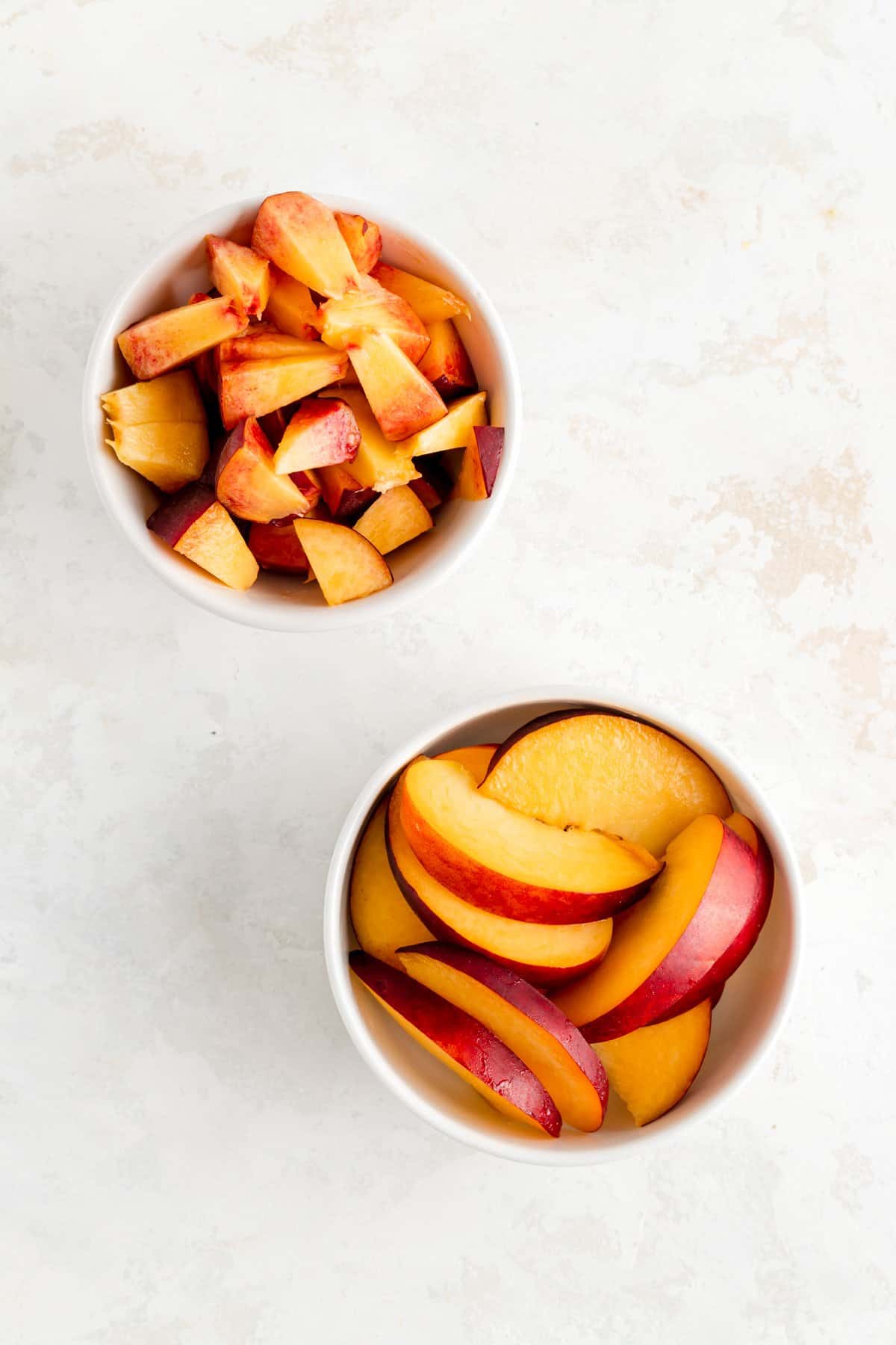 a bowl of diced peaches and a bowl of sliced peaches on a white background.