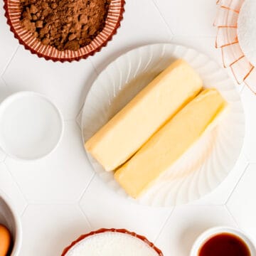 two sticks of butter on a white plate surrounded by other ingredients on a white background.