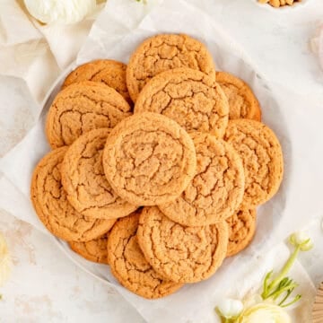 white plate of plain peanut butter cookies surrounded by ranunculus and ingredients in bowls.