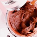 a glass mixer bowl of chocolate buttercream frosting sitting in the pink mixer.