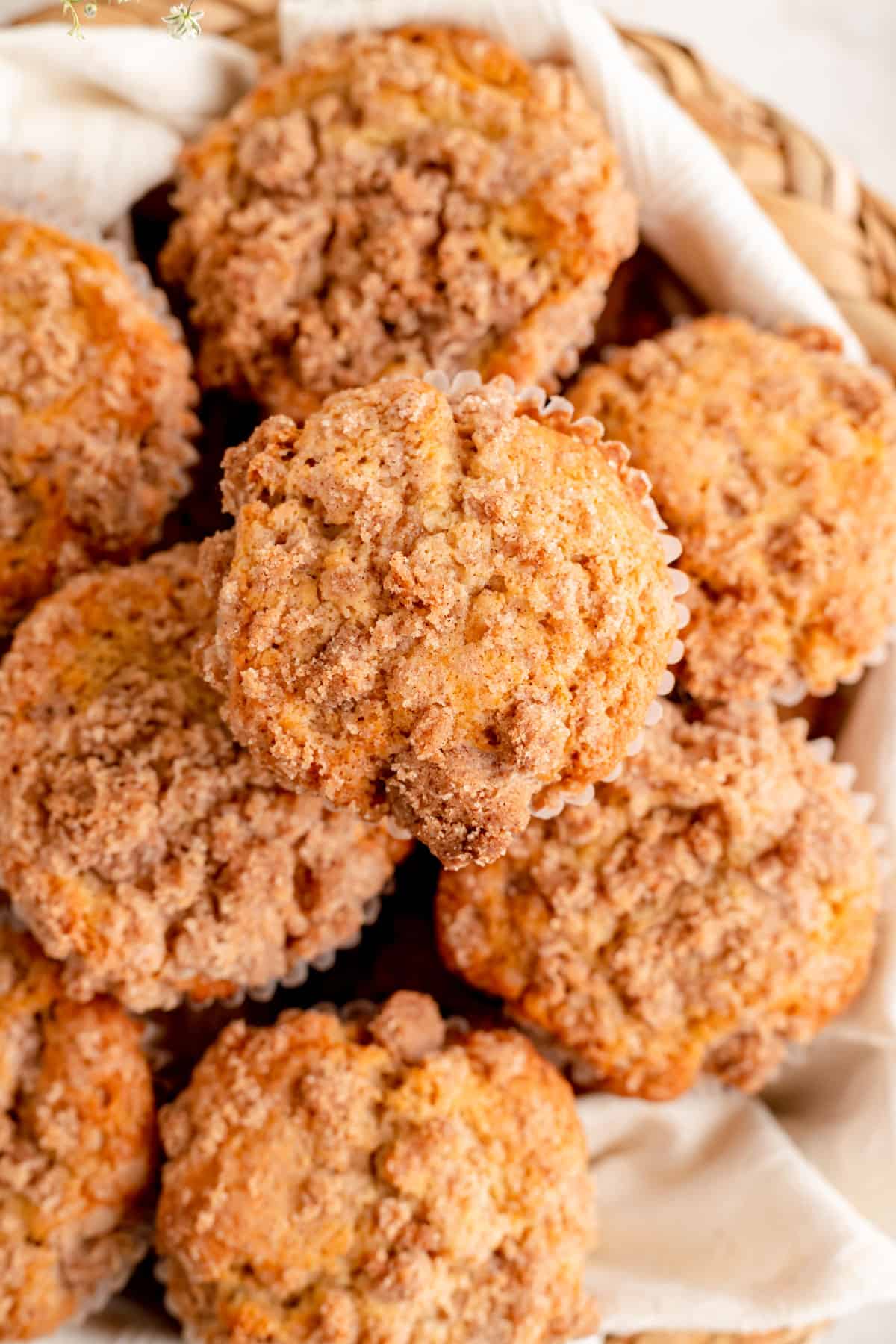 Overhead close up of cinnamon streusel topped muffins on white towel in woven basket.