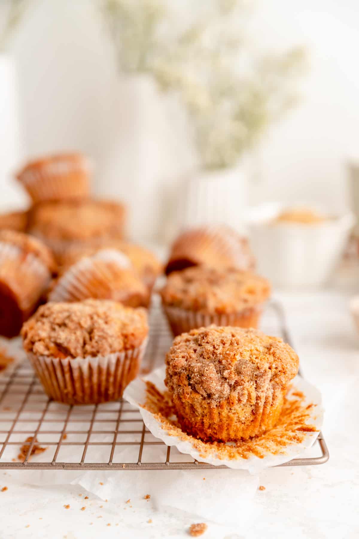 Cinnamon streusel topped muffin unwrapped on cooling rack with muffins in background.