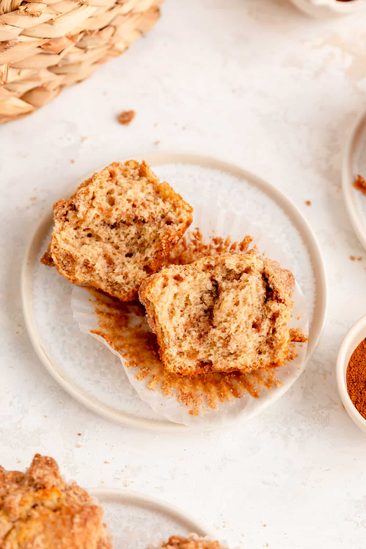 Cinnamon streusel muffin ripped in half on a muffin paper on white plate and background.