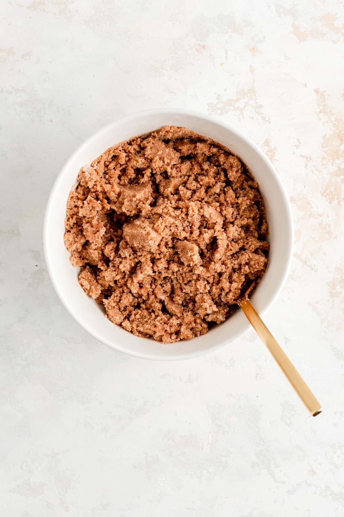 Fully blended cinnamon streusel in white bowl with gold fork on white background.