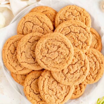 white plate of plain peanut butter cookies surrounded by ranunculus and ingredients in bowls.