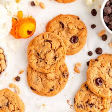 scattered chocolate chip peanut butter cookies with bowls of ingredients and flowers on table.