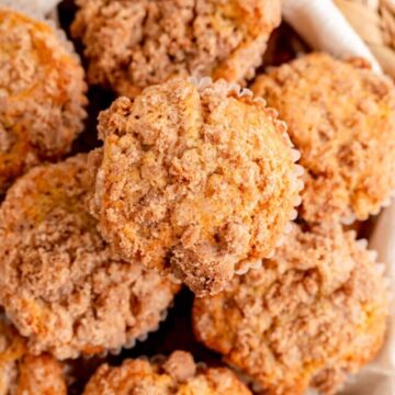 Overhead close up of cinnamon streusel topped muffins on white towel in woven basket.