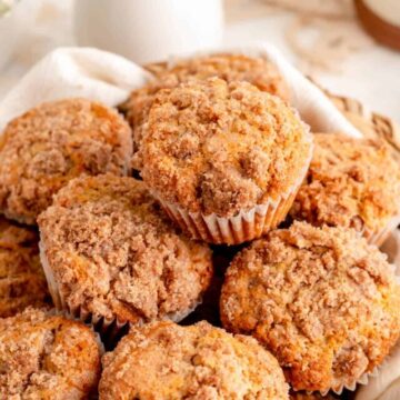45° angle close up of stacked cinnamon streusel muffins with white vase and flowers behind.