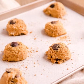 s'mores cookie dough balls spaced on a parchment paper on a champagne baking pan.