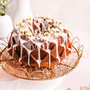 lemon bundt cake with lemon glaze and fresh flowers on a gold cake plate.