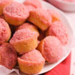 Strawberry sugar dusted Donut Muffins piled in a white bowl on a red towel.