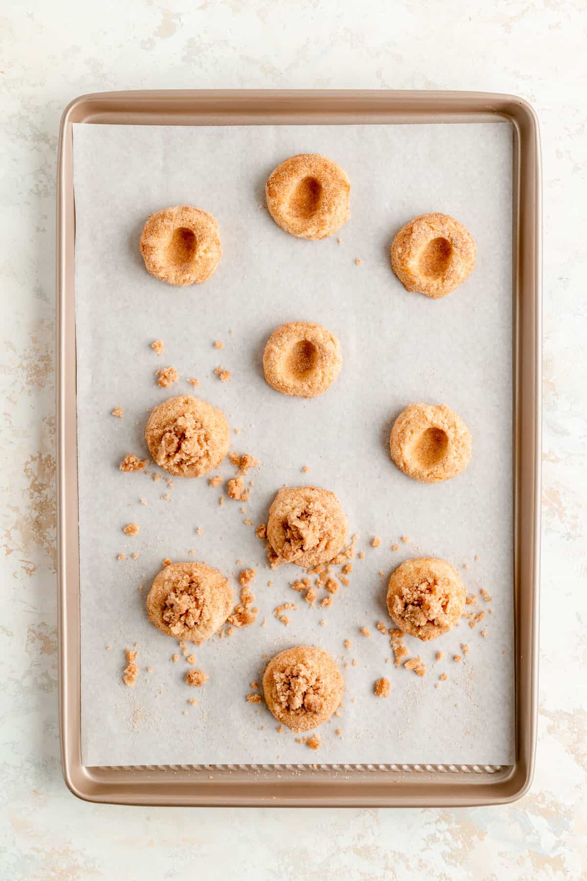 tan baking sheet with thumbprinted and filled coffee cake cookies spaced apart.