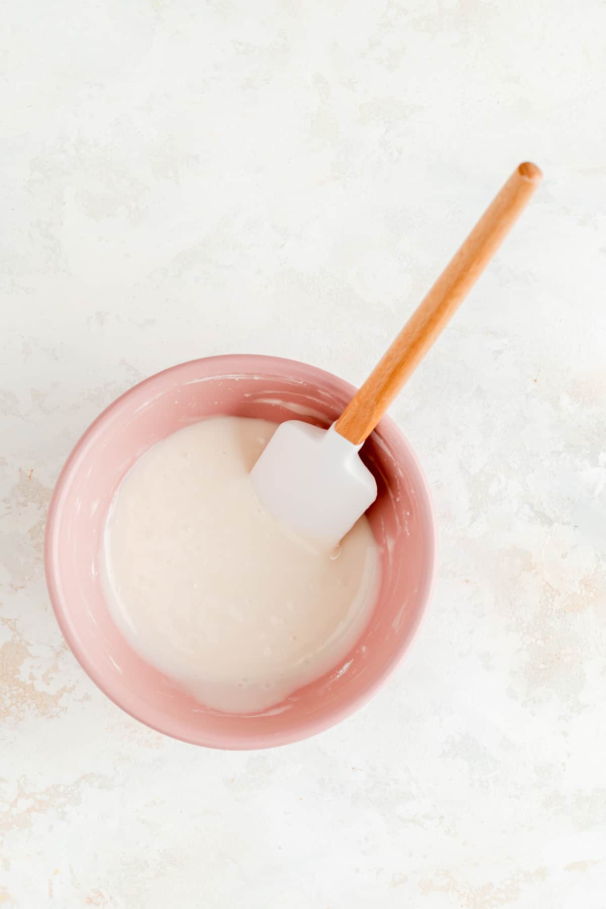 pink bowl with vanilla glaze and a white and wood spatula in it.