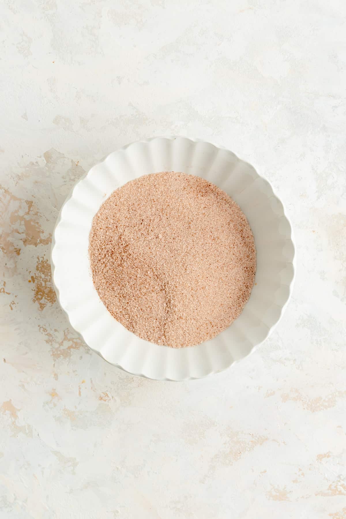 cinnamon and sugar in a white scalloped bowl and white plaster table.