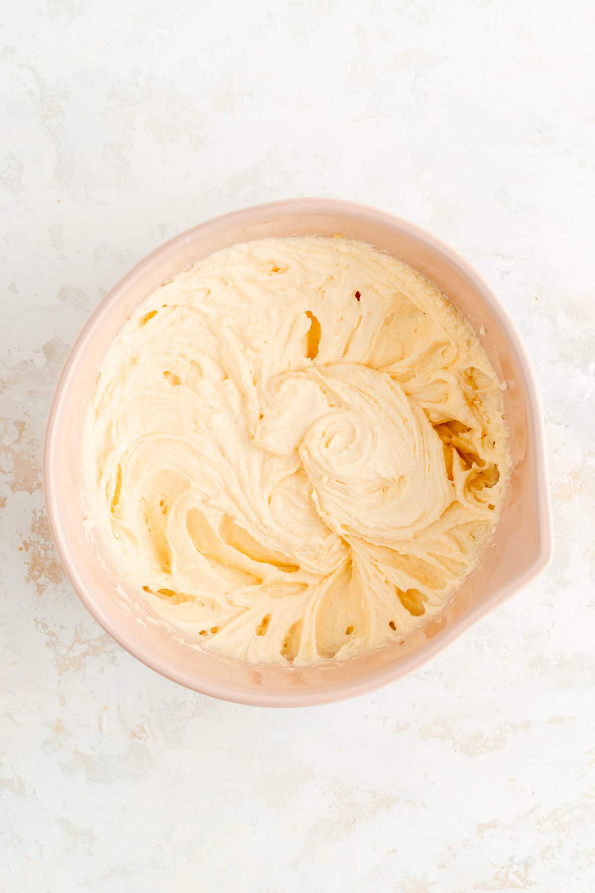 butter sugar and eggs mixed in a tan bowl on a white background.