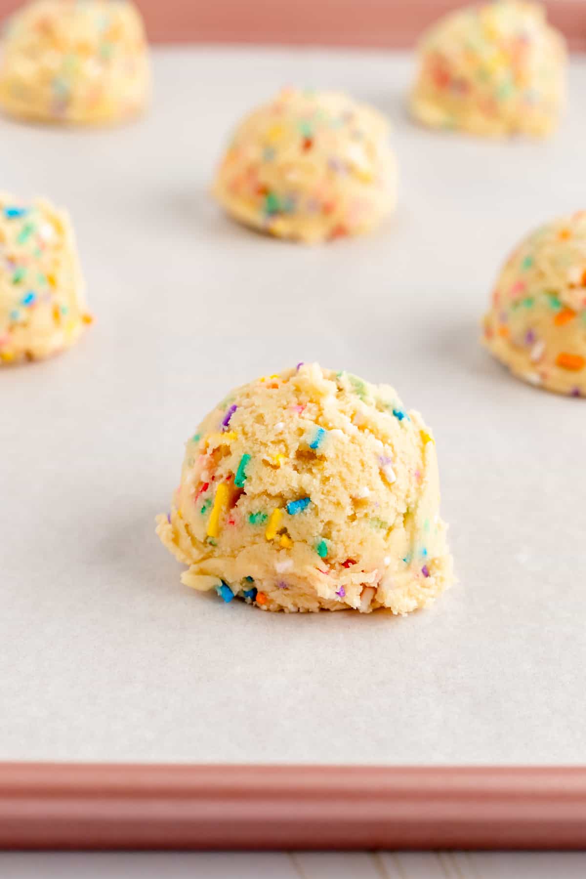 Scooped funfetti dough balls on a parchment lined pink baking pan.