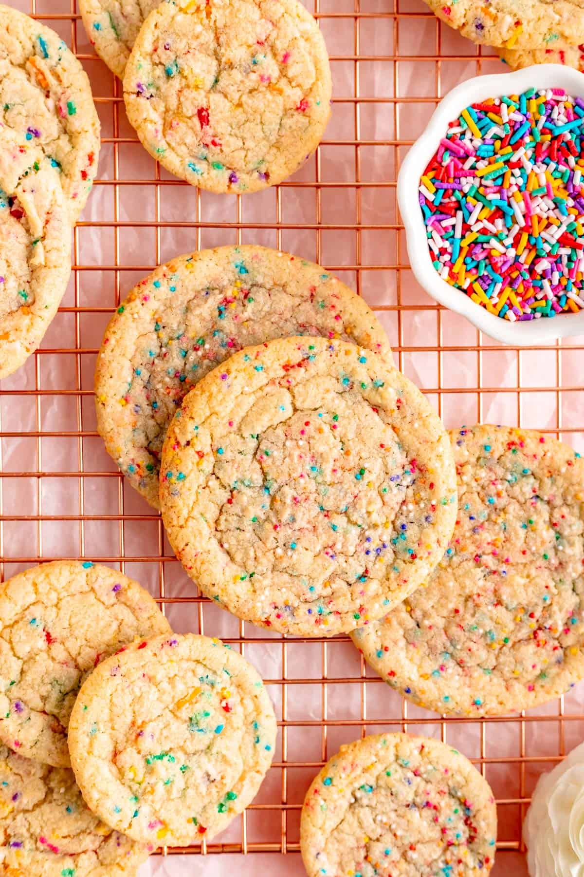 big and little cookies with round and stick sprinkles scattered on copper wire rack.