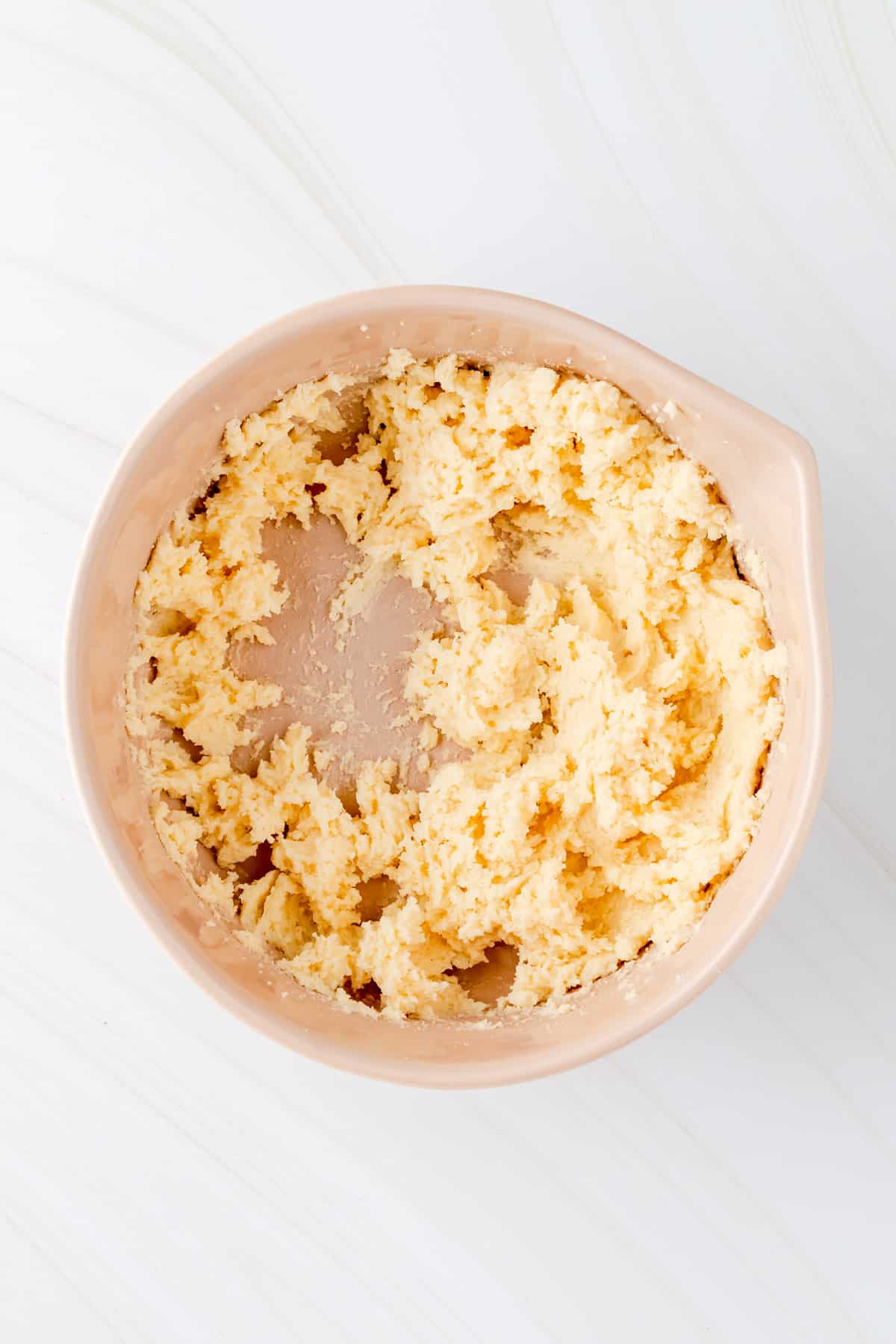 Cream butter and sugar in a tan mixing bowl on white background.