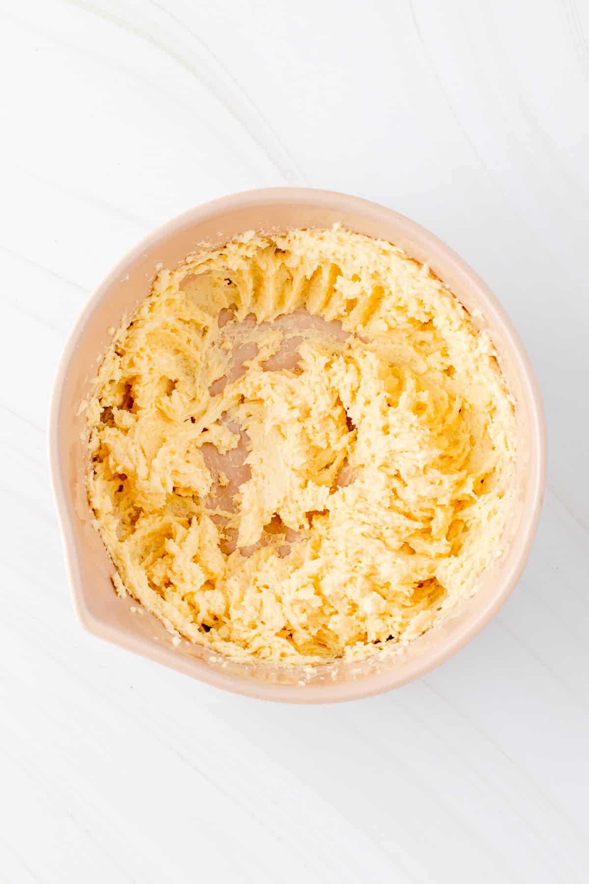 Egg butter and sugar whipped in a tan mixing bowl on white background.