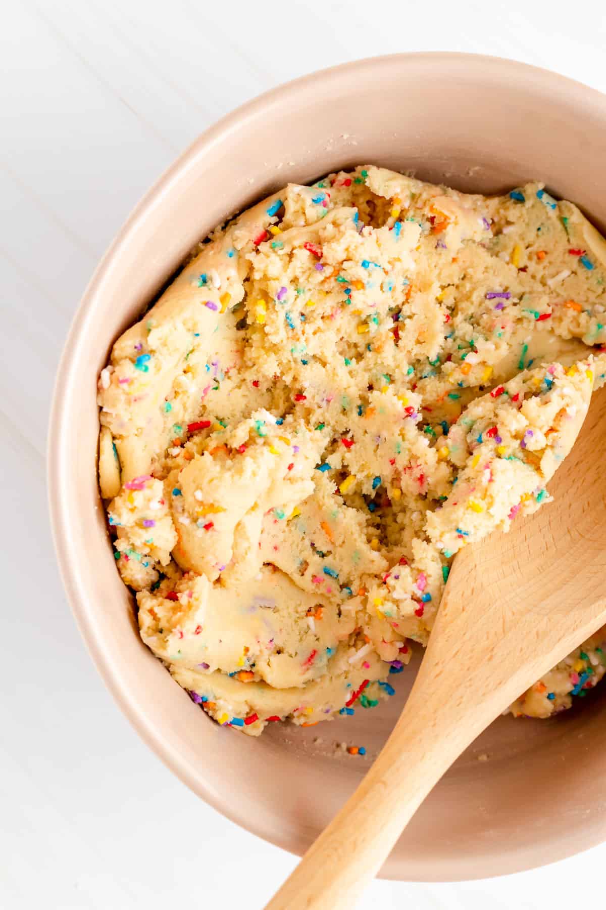 Close up of sprinkle filled funfetti cookie dough in tam mixing bowl with wooden spoon.