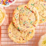 Close up of three funfetti cookies on copper wire rack with bowl of sprinkles and flowers.