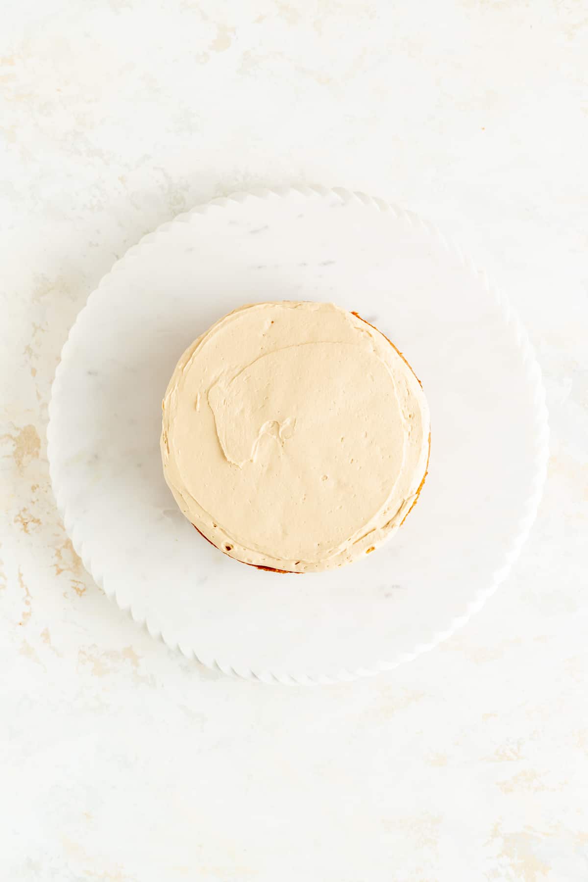 Overhead view of first biscoff frosting layer on white marble plate and white background.