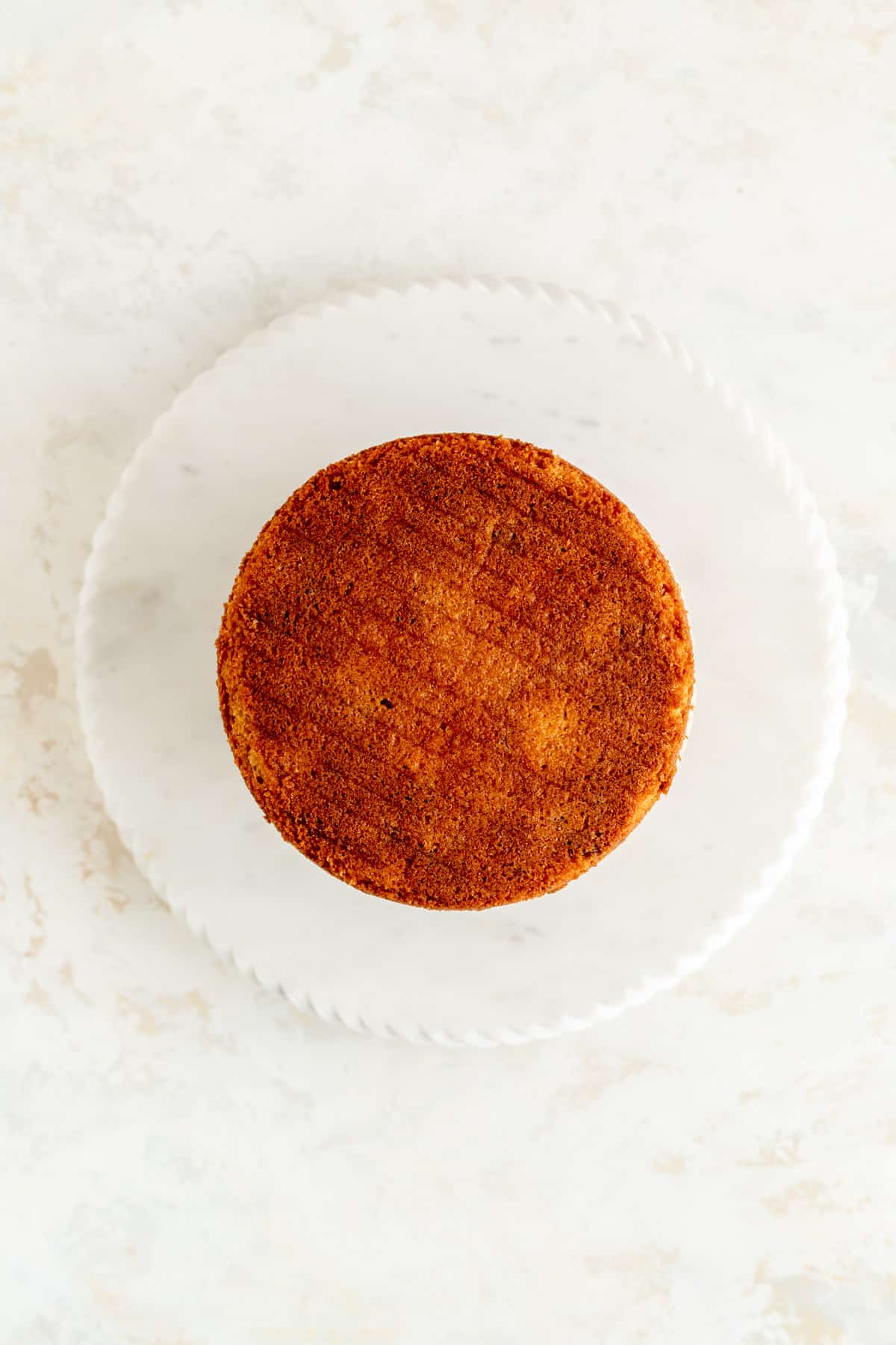 Overhead view of upside down top cake layer on white marble plate and white background.
