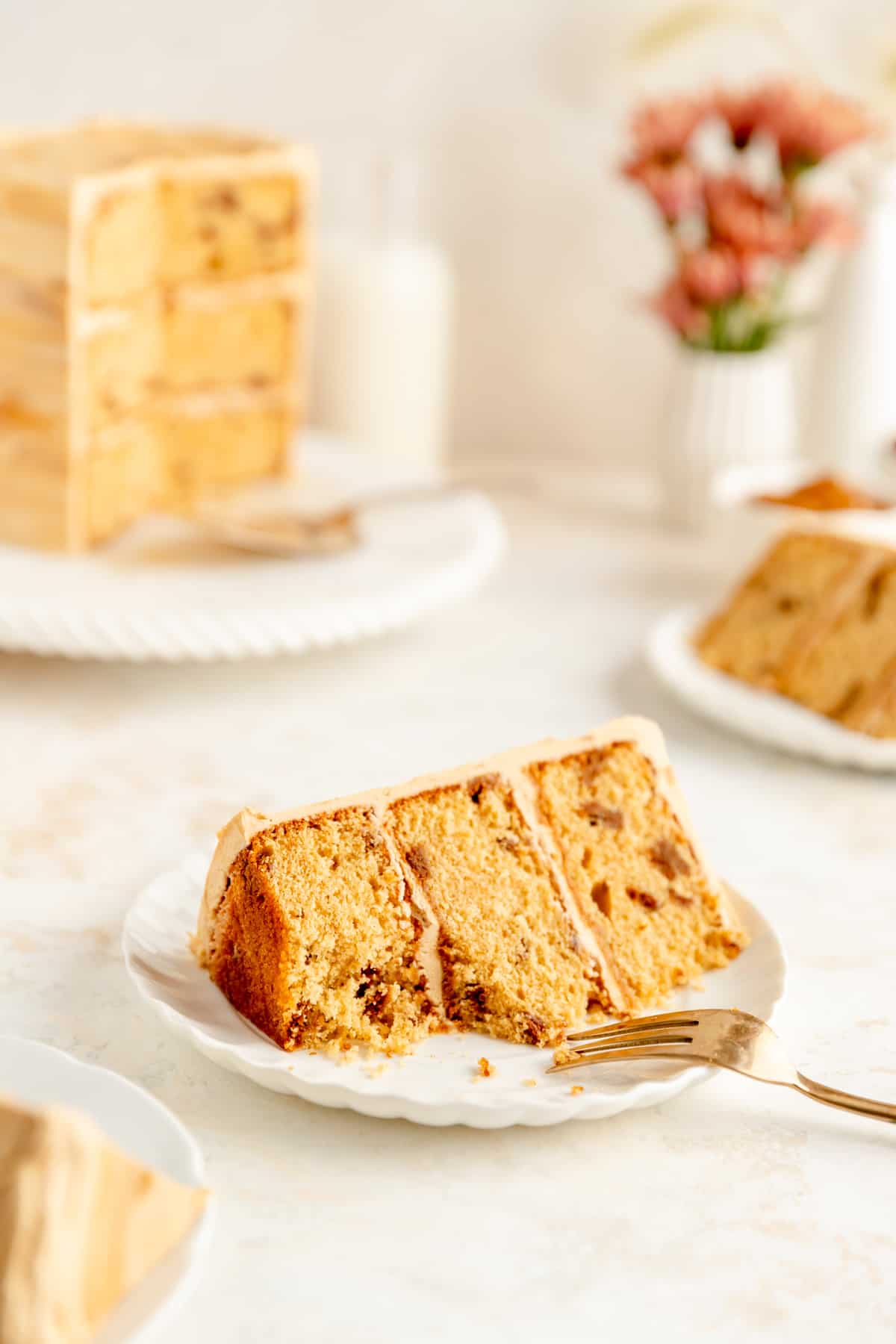 Plated biscoff cake slice with a bite out and gold fork with whole cake in background.